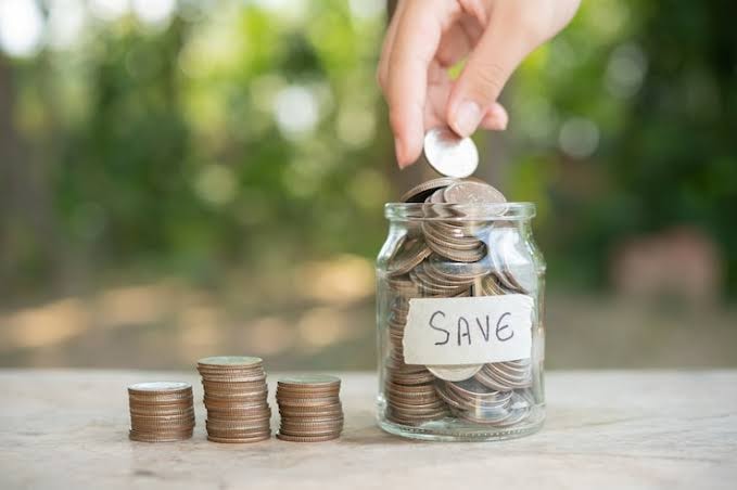 Hand placing coin into savings jar representing financial assistance